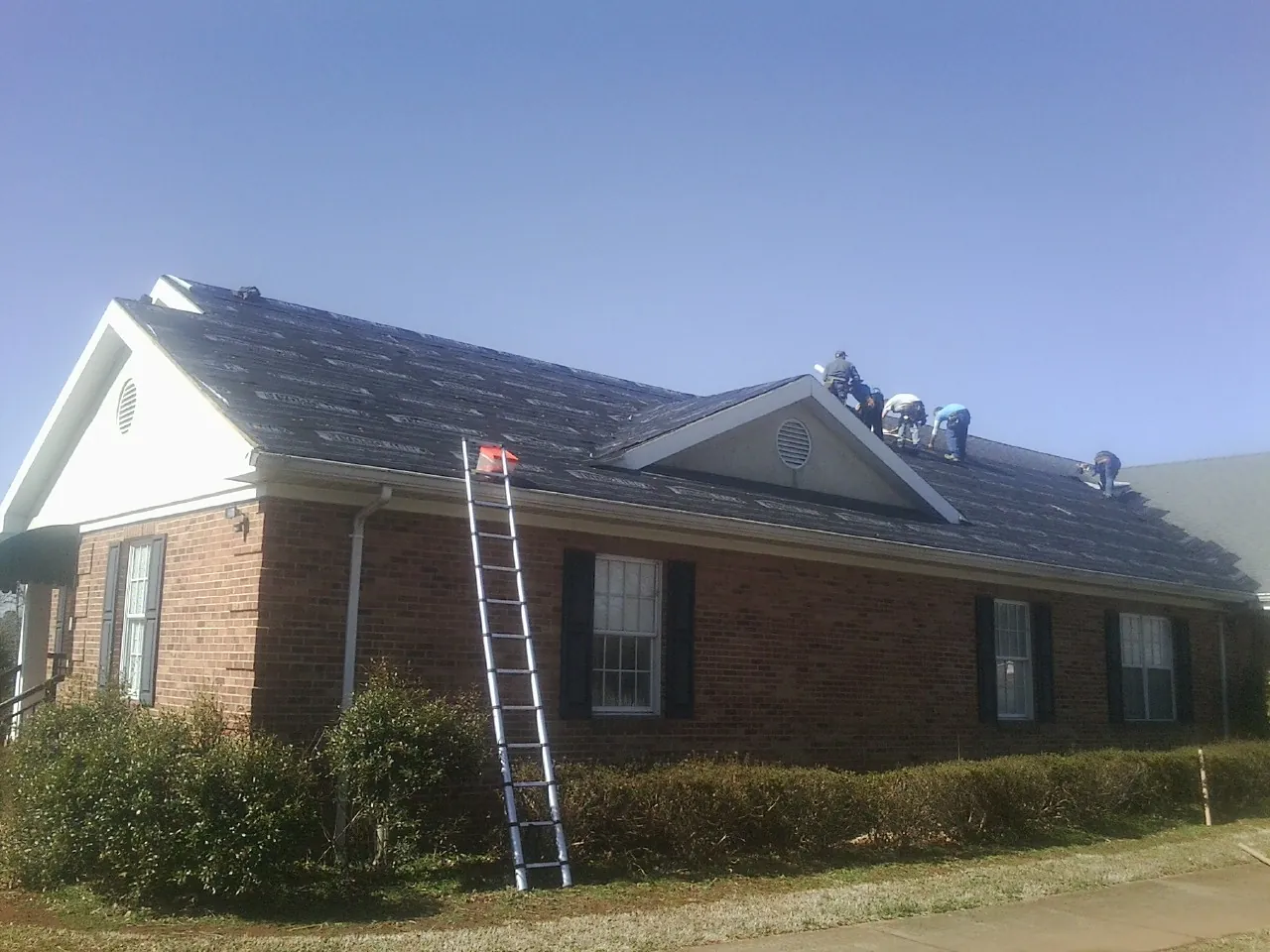 Crew tearing shingles off a brick ranch roof with a ladder set — Emergency Roof Repair work by our crew in Batavia