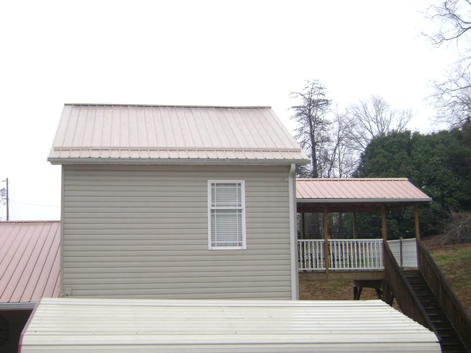 Tan metal roofs on a two story addition and attached porch, from a Roof Replacement job in Batavia
